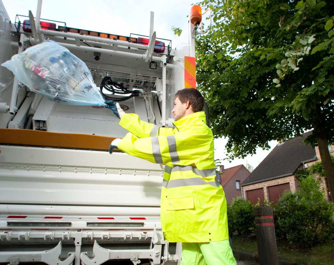 operative in safety clothing throwing a bag into a recycling collection vehicle